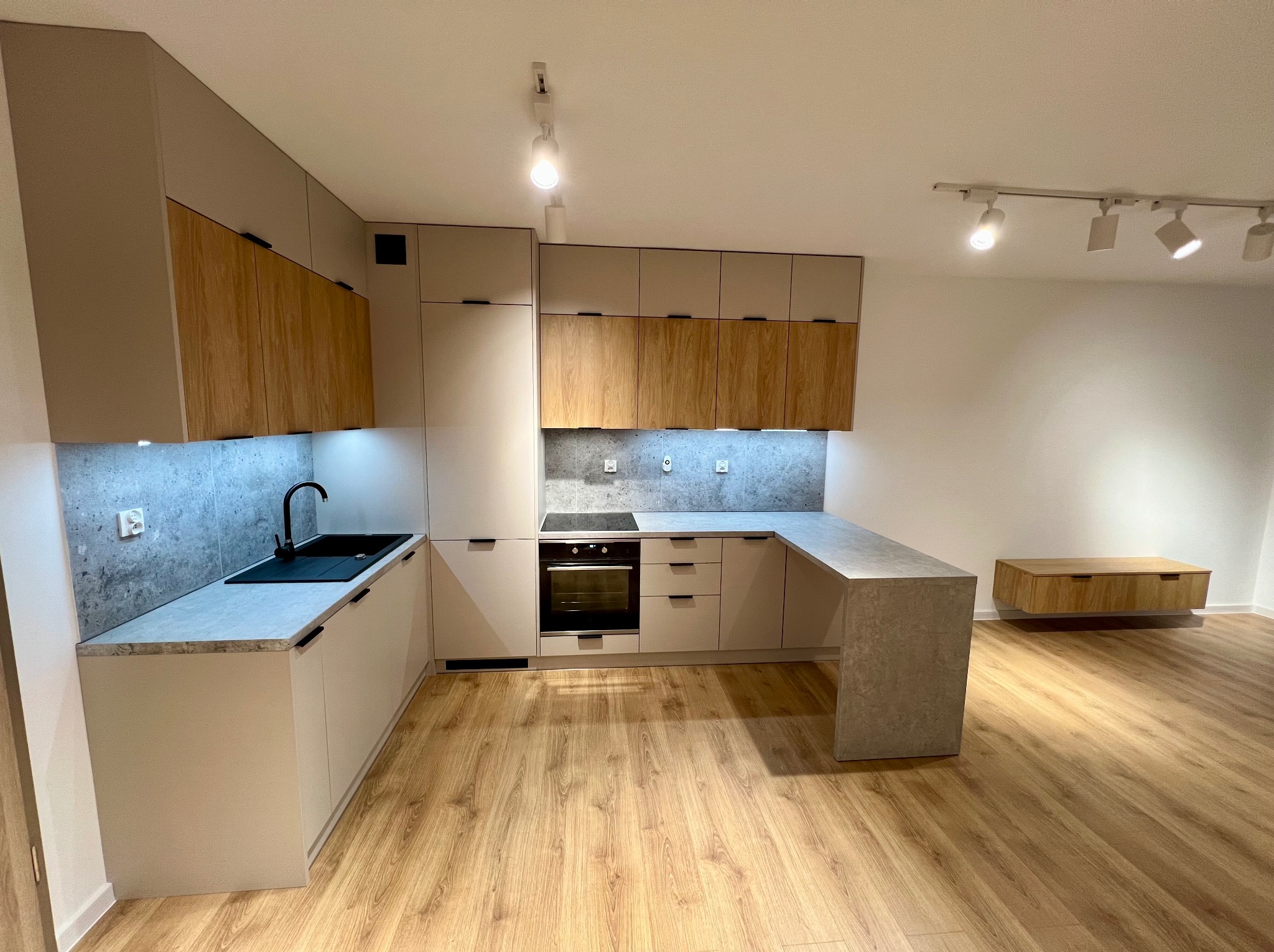 Nowoczesna kuchnia z drewnianymi i beżowymi frontami, szarym blatem i podświetleniem LED, na podłodze panele imitujące drewno.