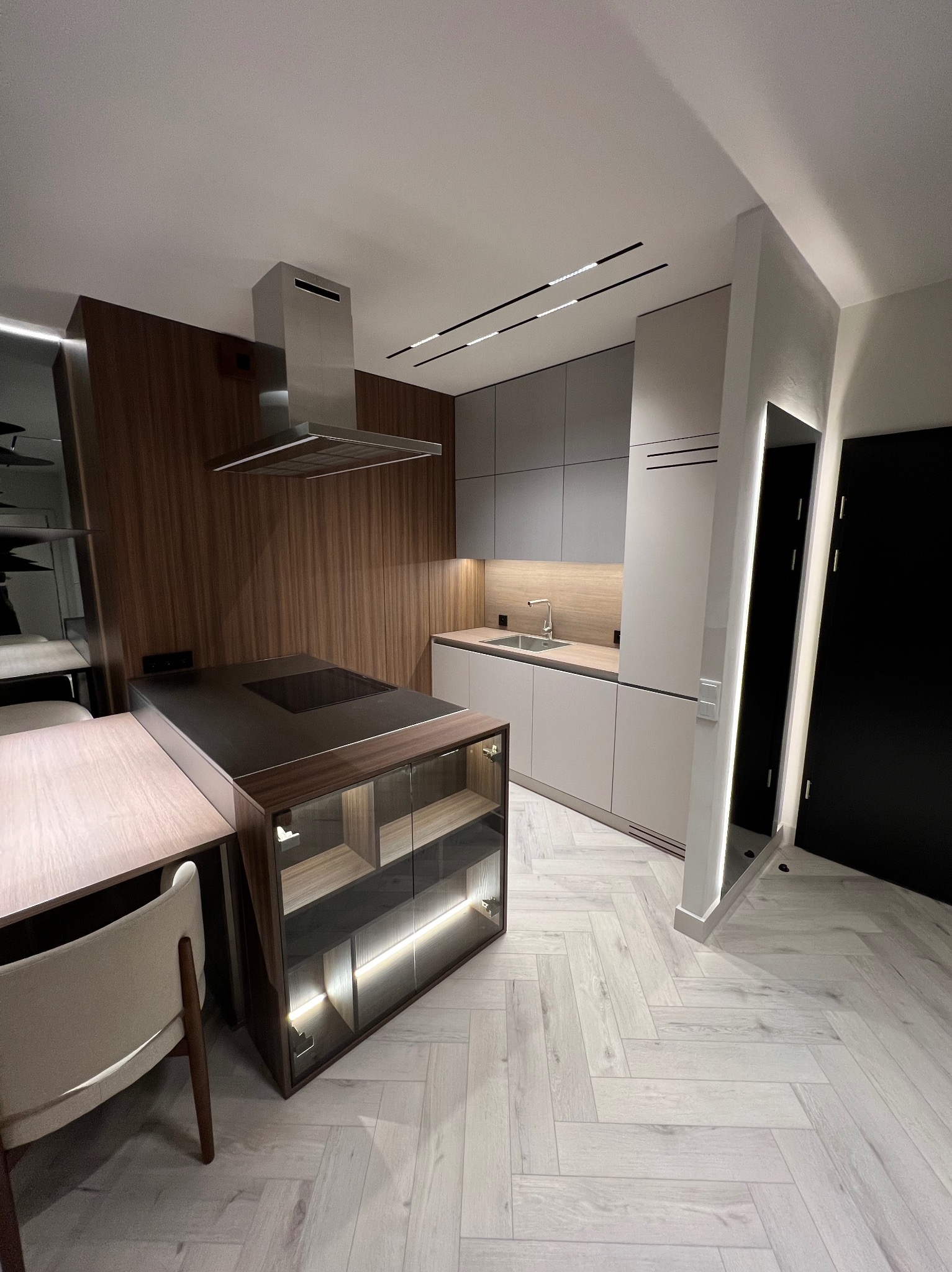 Nowoczesna kuchnia z wyspą i drewnianymi akcentami, oświetleniem LED i podłogą ułożoną w jodełkę.