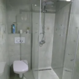 Nowoczesna kabina prysznicowa walk-in z odpływem liniowym, zamontowana w wykończonej łazience z jasnymi płytkami imitującymi marmur i podwieszaną toaletą.