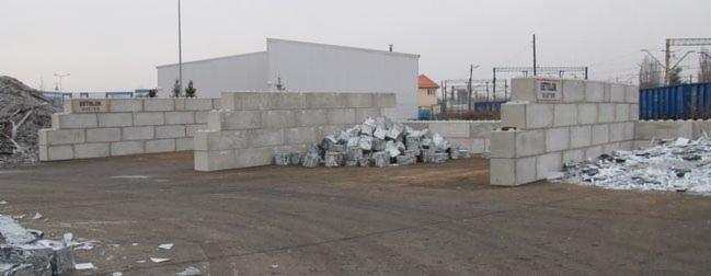 Magazyn prefabrykatów betonowych typu boks, z widocznymi elementami składowanymi luzem na placu, w tle budynki magazynowe i infrastruktura kolejowa.