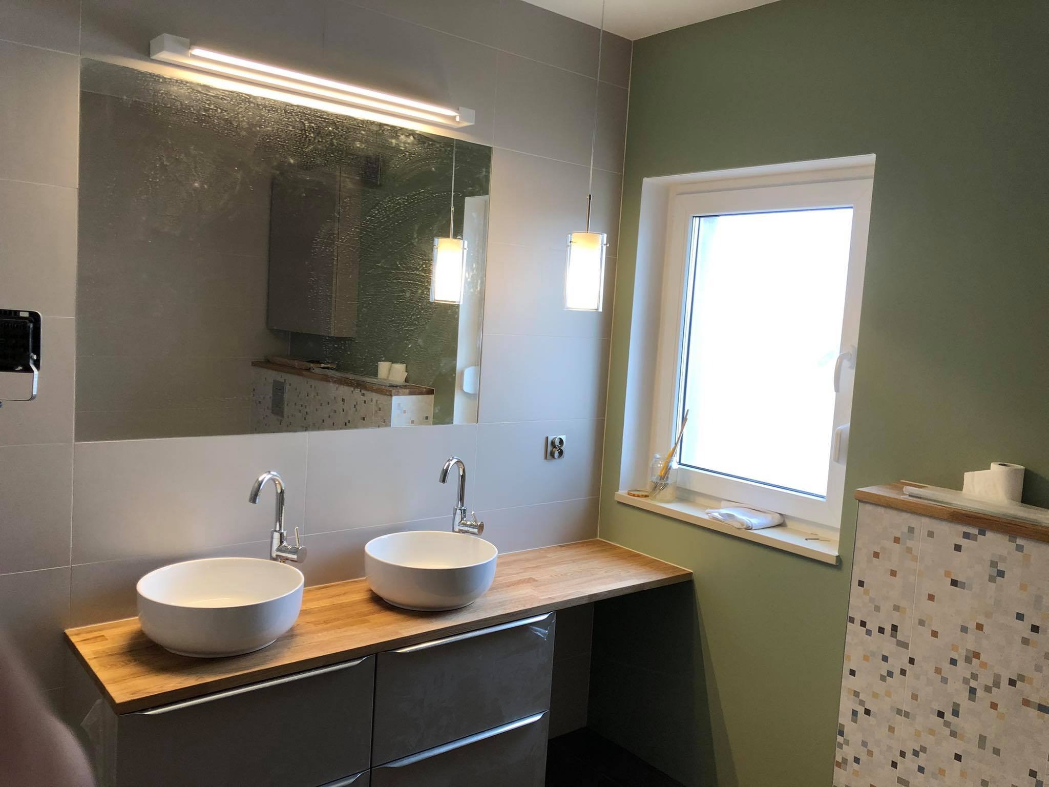 Nowoczesna łazienka z dwoma okrągłymi umywalkami nablatowymi, drewnianym blatem, szarą szafką podumywalkową i dużym lustrem z oświetleniem LED.
