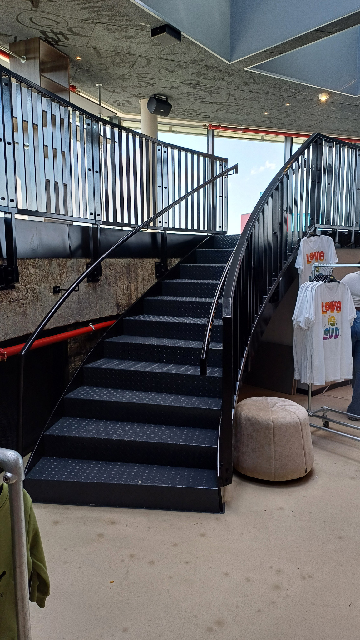 Czarne metalowe schody z balustradą w nowoczesnym wnętrzu, widoczne elementy wystroju sklepu z odzieżą.