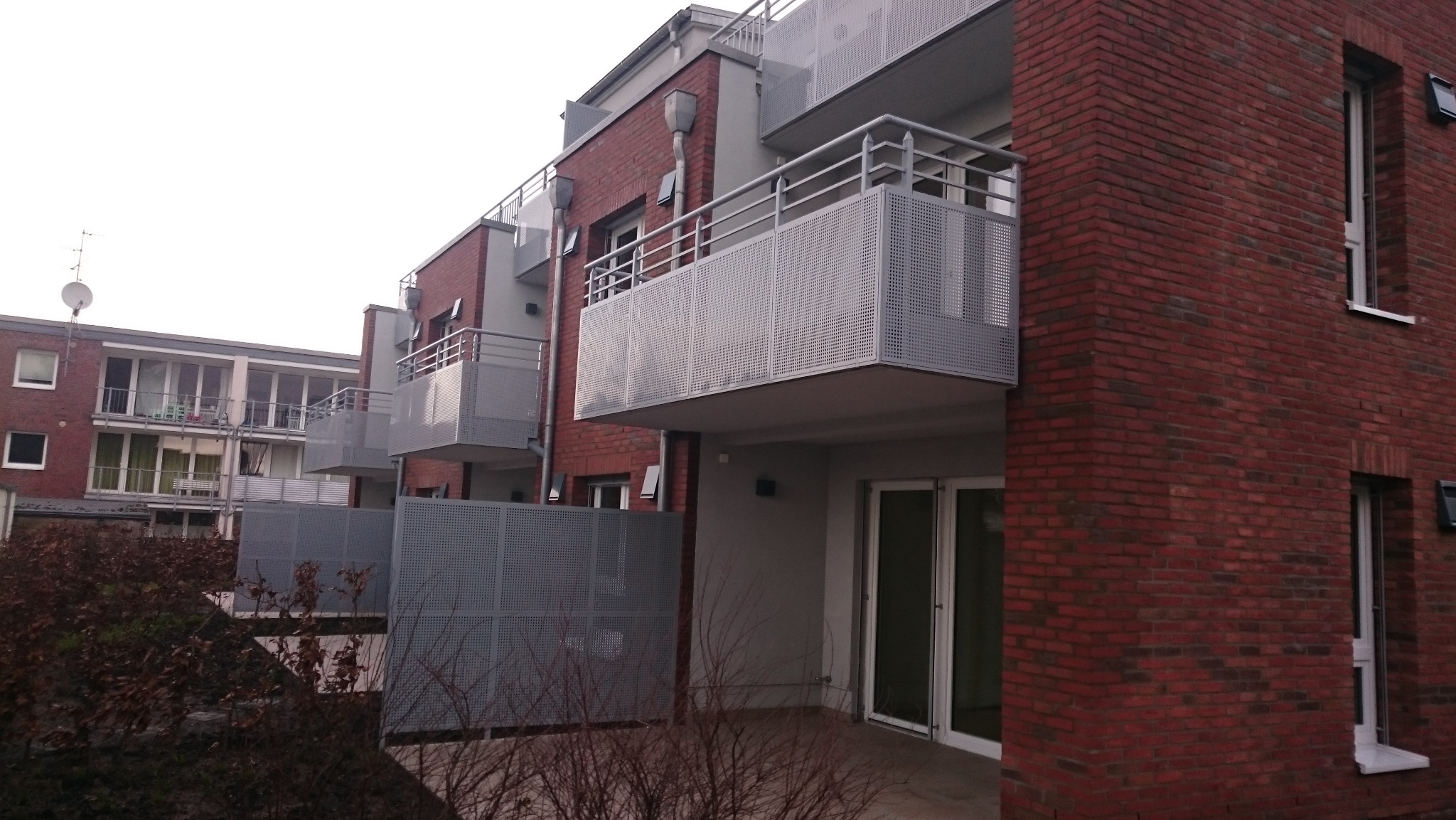 Nowoczesny budynek wielorodzinny z cegły klinkierowej z balkonami z perforowanej blachy, widok z dołu na elewację i balustrady.