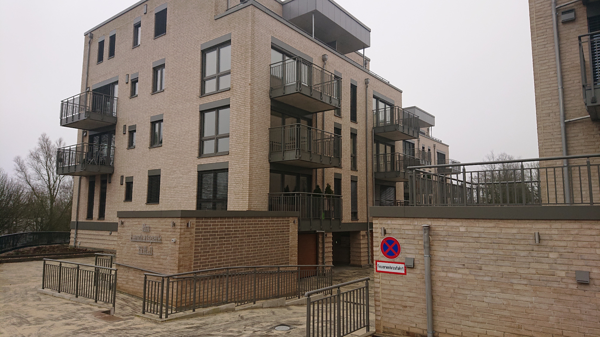 Nowoczesny budynek wielorodzinny z balkonami z balustradami w Drawno, widok z poziomu chodnika na elewację z jasnej cegły.