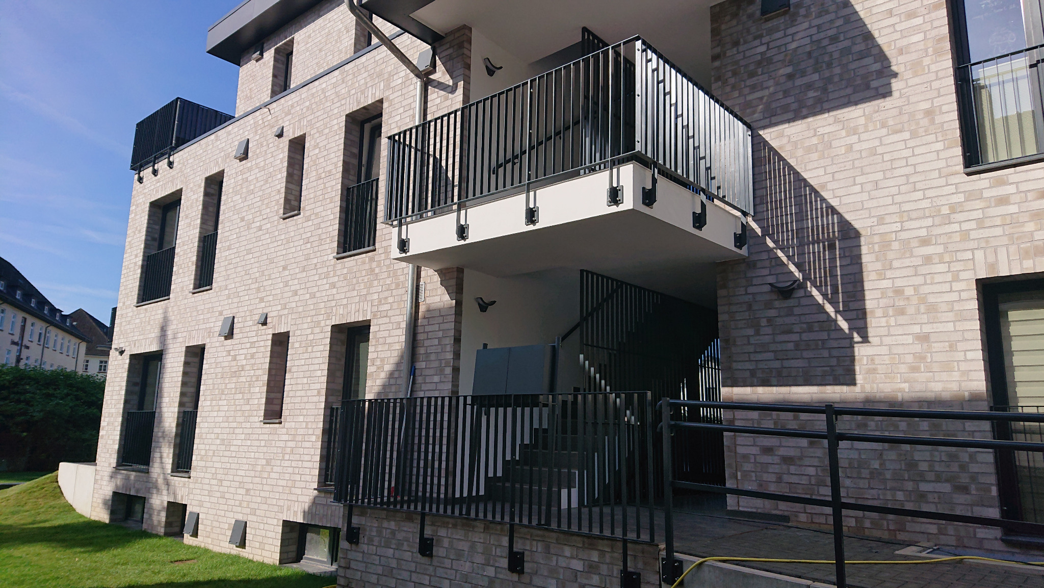 Nowoczesny budynek z jasnej cegły z balkonem i schodami zabezpieczonymi czarnymi, metalowymi balustradami. Widoczne elementy mocujące balustrady do ściany.