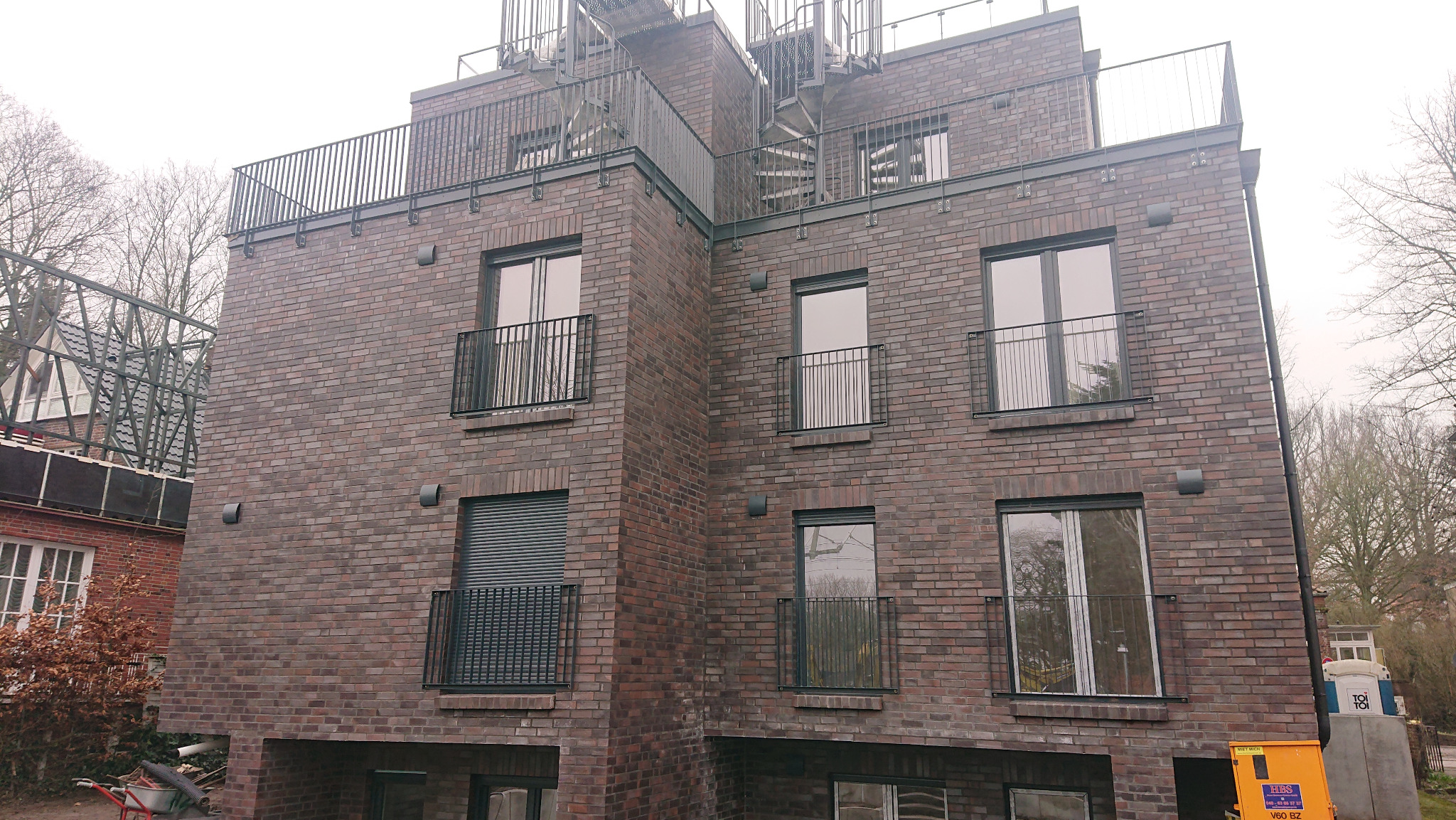 Nowoczesny budynek z ciemnej cegły z balkonami z metalowymi balustradami i zewnętrznymi schodami spiralnymi.