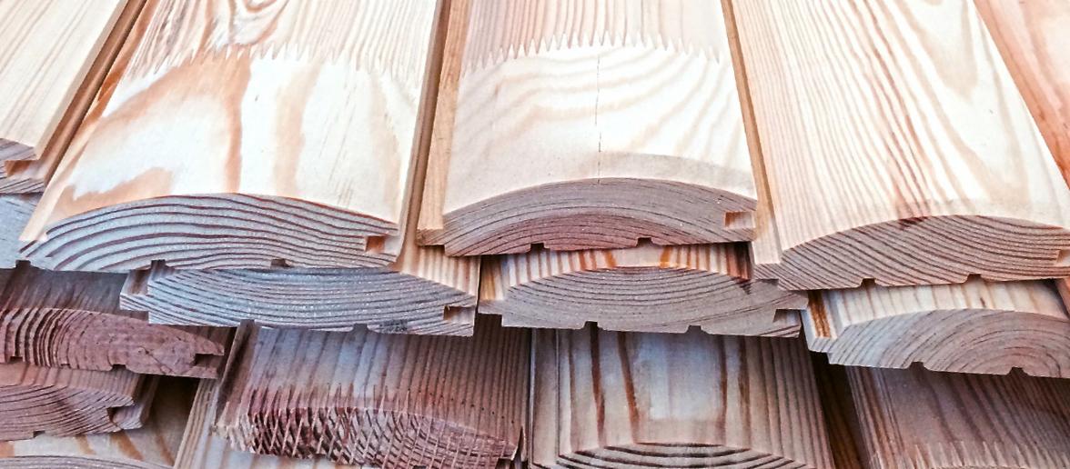 Profilowane deski z jasnego drewna ułożone jedna na drugiej, widoczne słoje i rowki montażowe.