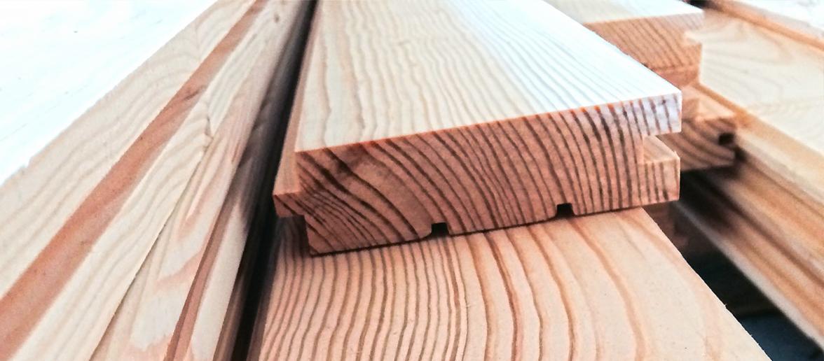 Stos drewnianych desek z wyfrezowanymi wpustami i wypustami, widoczne słoje drewna.