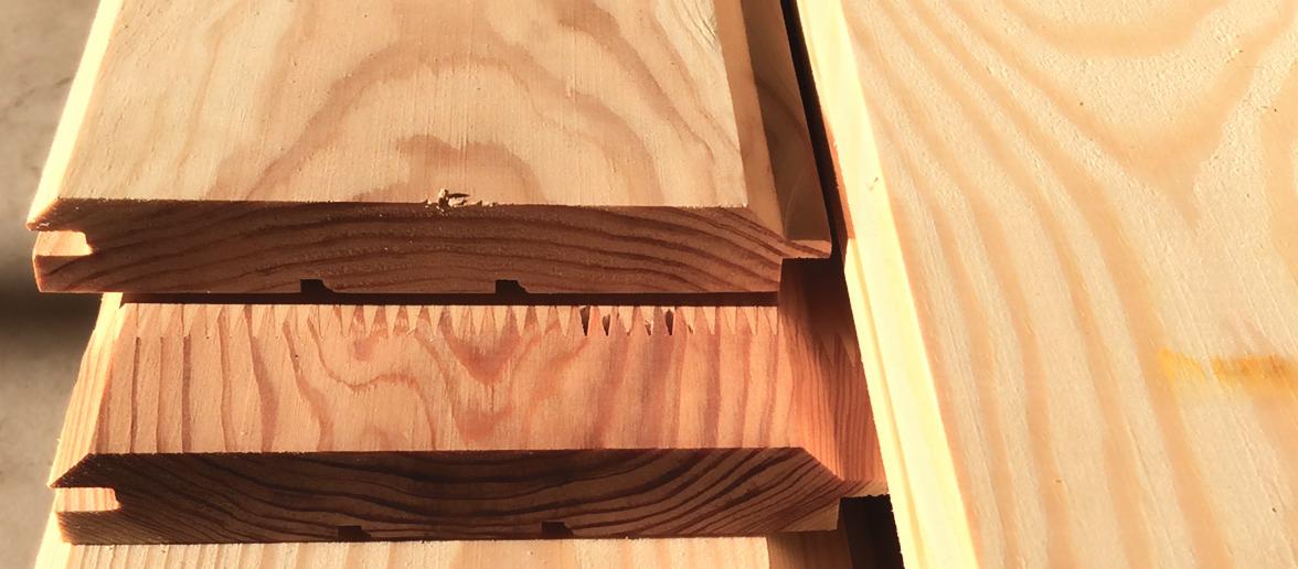 Profilowane deski z jasnego drewna z widocznymi połączeniami na pióro i wpust, ułożone warstwowo.