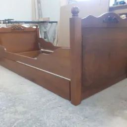 Drewniane łóżko dziecięce w trakcie montażu w warsztacie, widoczne elementy dekoracyjne i szuflada, surowy beton na podłodze.