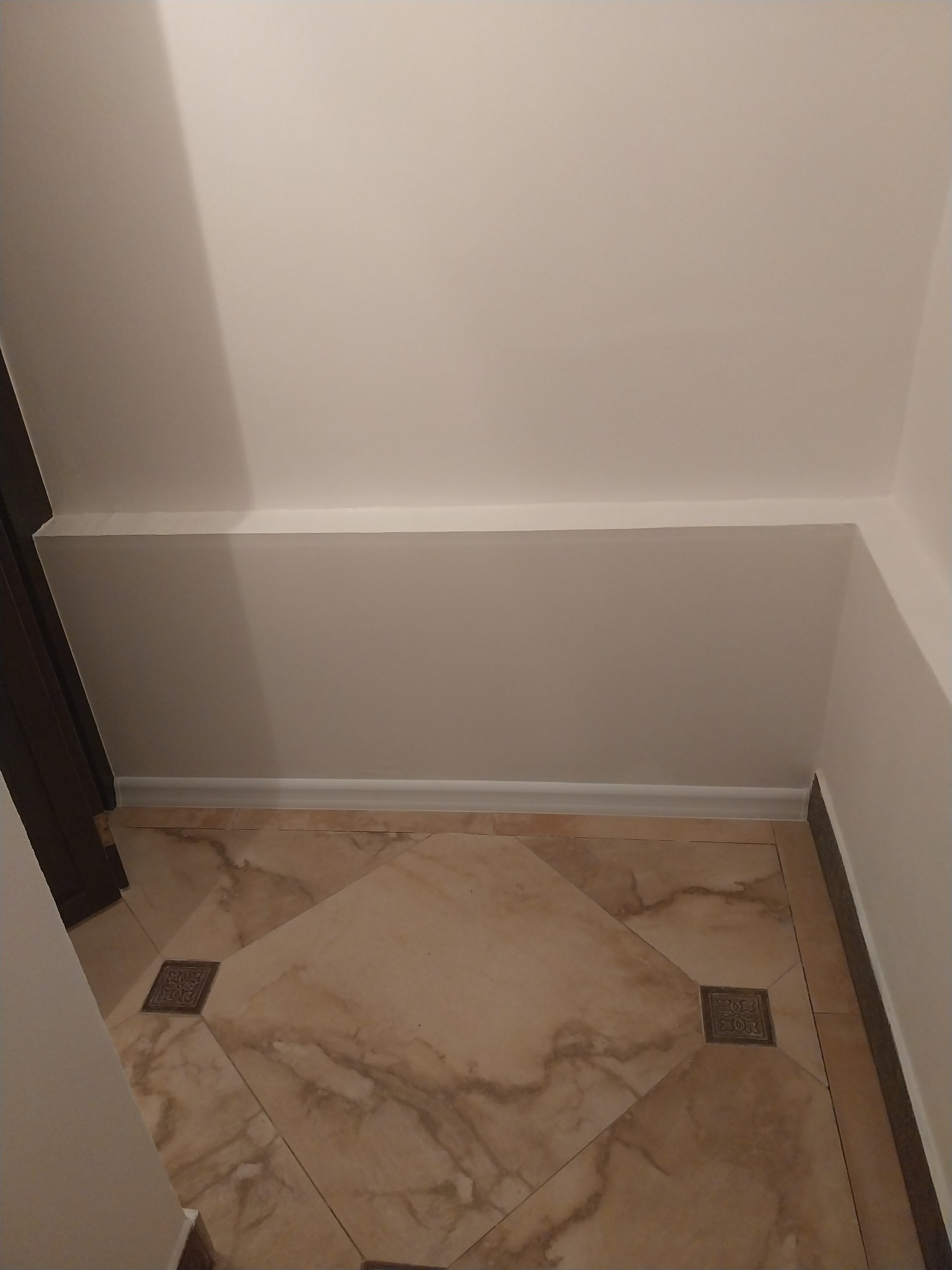 Świeżo pomalowane białe ściany i sufit w rogu pomieszczenia, widoczne dekoracyjne listwy przypodłogowe i fragment marmurowej podłogi z ozdobnymi kwadratami, minimalizm.