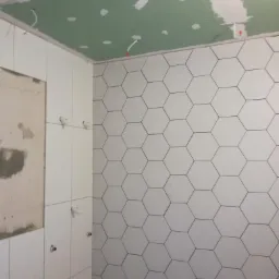 Montaż heksagonalnych płytek ściennych w łazience, widoczne niedokończone prace, surowy sufit z widocznymi przewodami elektrycznymi, częściowo położone płytki.