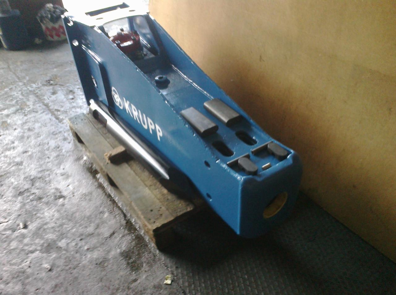 Niebieski młot hydrauliczny marki Krupp, umieszczony na drewnianej palecie w warsztacie, widoczny srebrny grot