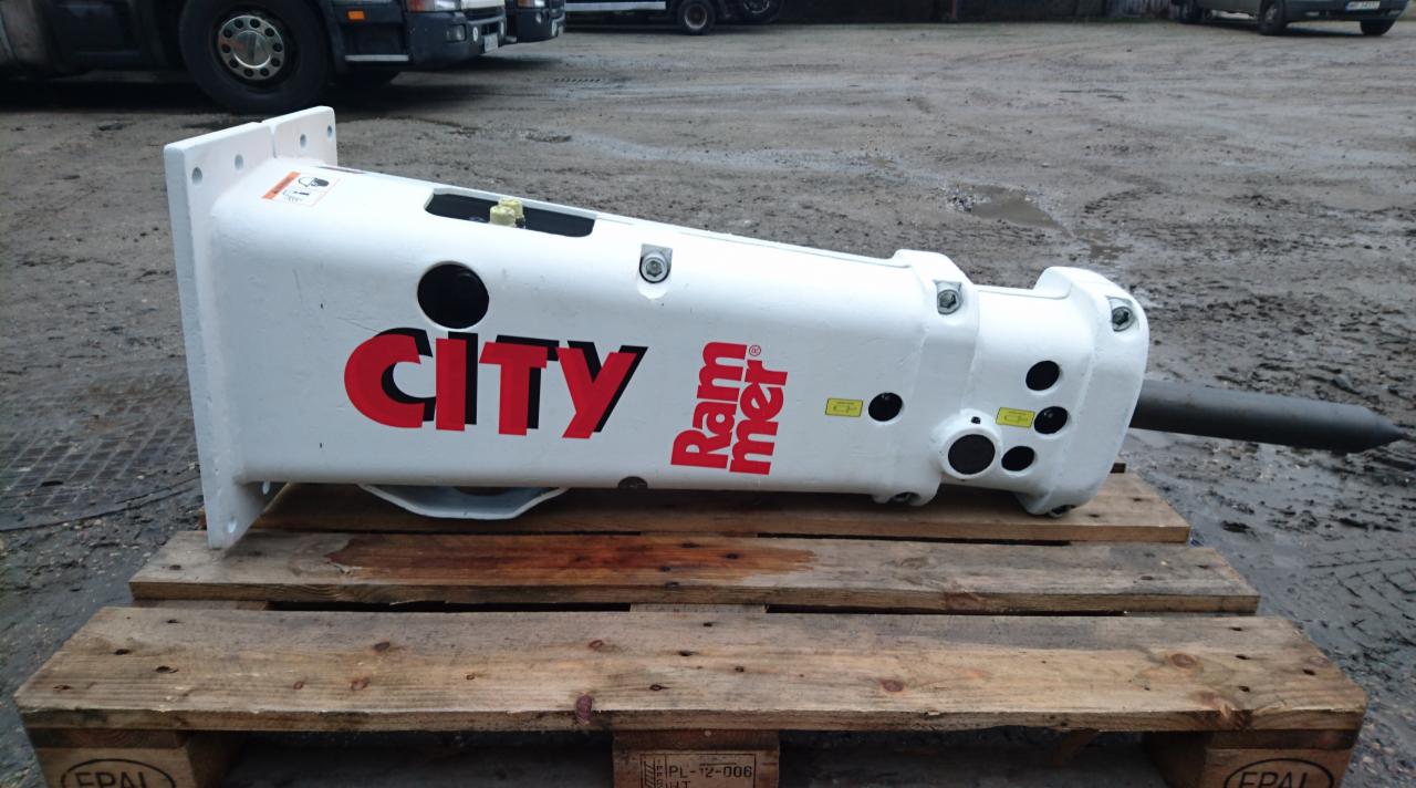 Hydrauliczny młot wyburzeniowy City Rammer na drewnianej palecie, z fragmentem ciężarówki w tle.