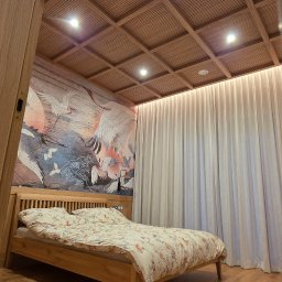 Magic Meble - Drewniane wykończenie sypialni: parkiet, łóżko z zagłówkiem, sufit kasetonowy z oświetleniem. Na ścianie fototapeta z motywem żurawi. Lekkie, zwiewne zasłony.