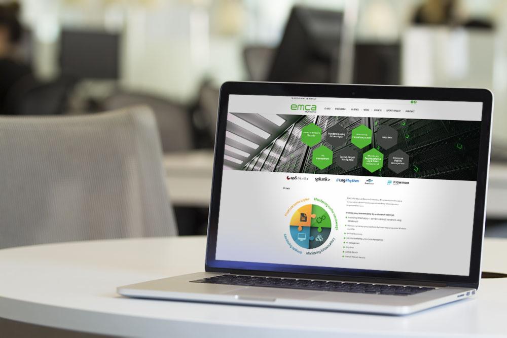 Laptop wyświetlający stronę internetową IT EMCA na białym stole w biurze, z widocznymi elementami graficznymi i logo.