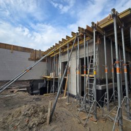 DKK PROPERTY INVESTMENTS SPÓŁKA Z OGRANICZONĄ ODPOWIEDZIALNOŚCIĄ - Budowa domu z betonu komórkowego: ściany zbrojone szalunkami i podporami stalowymi, widoczne detale konstrukcyjne i etap prac na tle błękitnego nieba.