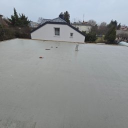 DKK PROPERTY INVESTMENTS SPÓŁKA Z OGRANICZONĄ ODPOWIEDZIALNOŚCIĄ - Świeżo wylany, szary strop budynku jednorodzinnego w trakcie budowy, widok z góry. W tle zabudowa mieszkalna i pochmurne niebo.