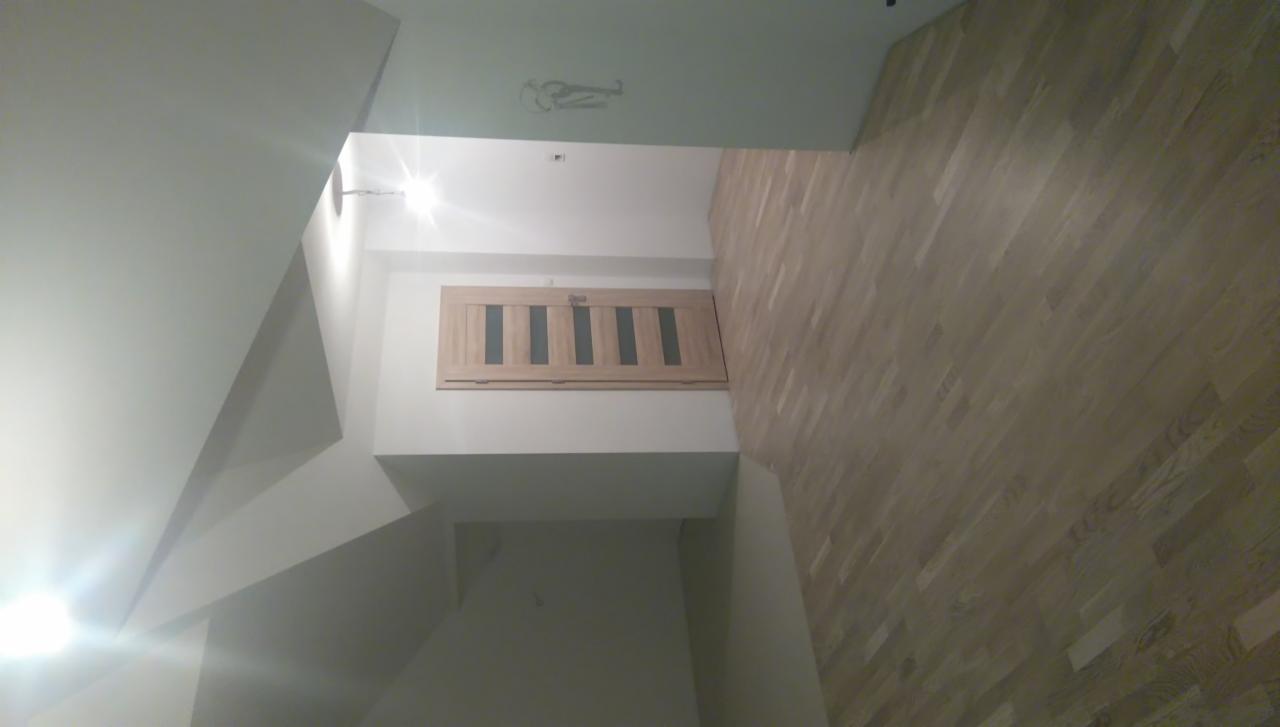 Wnętrze mieszkania z drewnianą podłogą i drzwiami z przeszkleniami, widoczne białe ściany i sufit z oświetleniem punktowym.