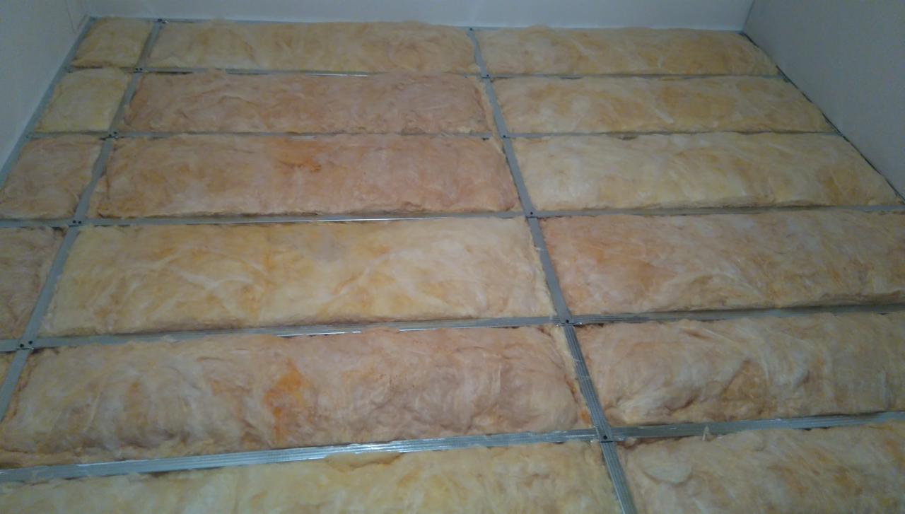 Montaż izolacji z wełny mineralnej w metalowym stelażu na ścianie podczas remontu.