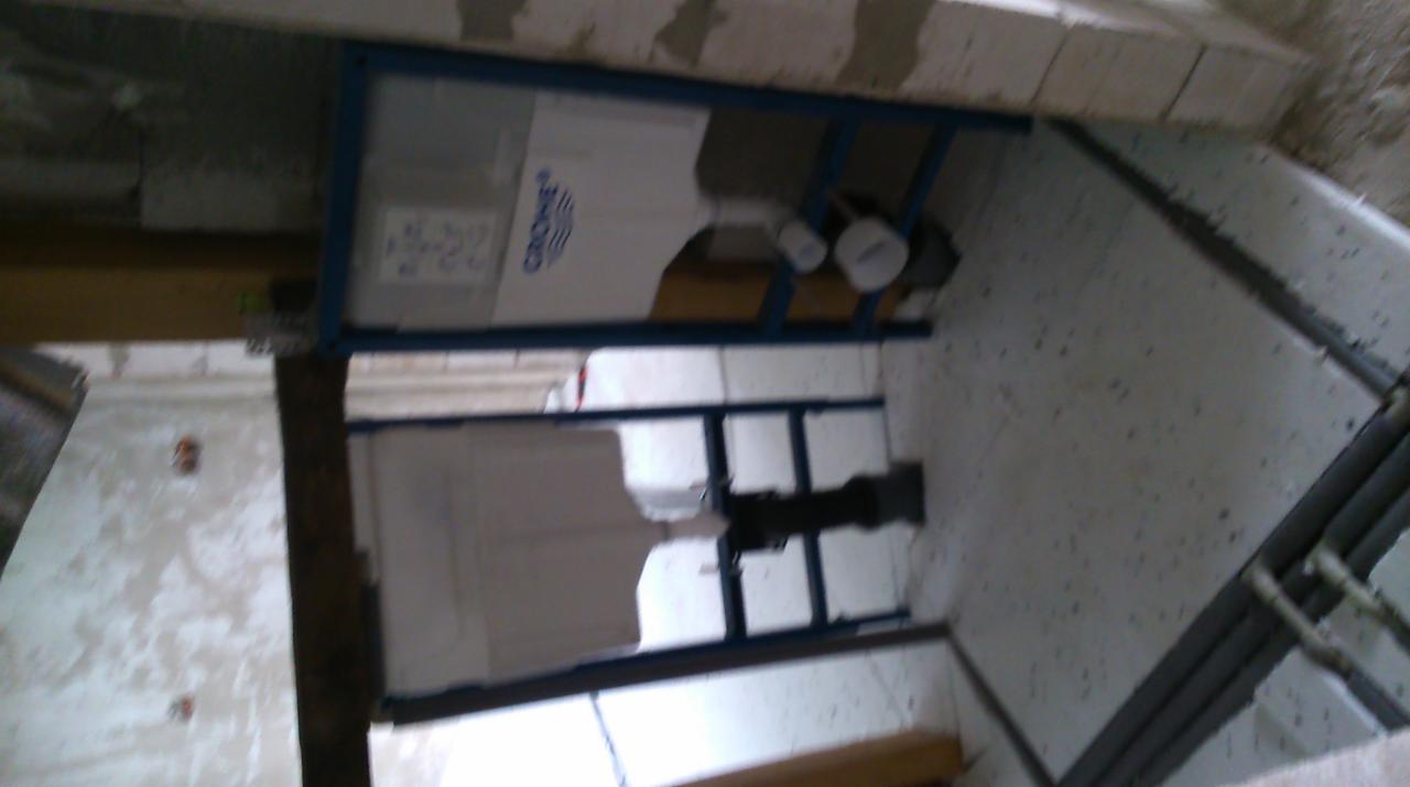 Montaż stelaża podtynkowego Grohe w surowej łazience z widocznymi rurami i niedokończonymi ścianami z bloczków.