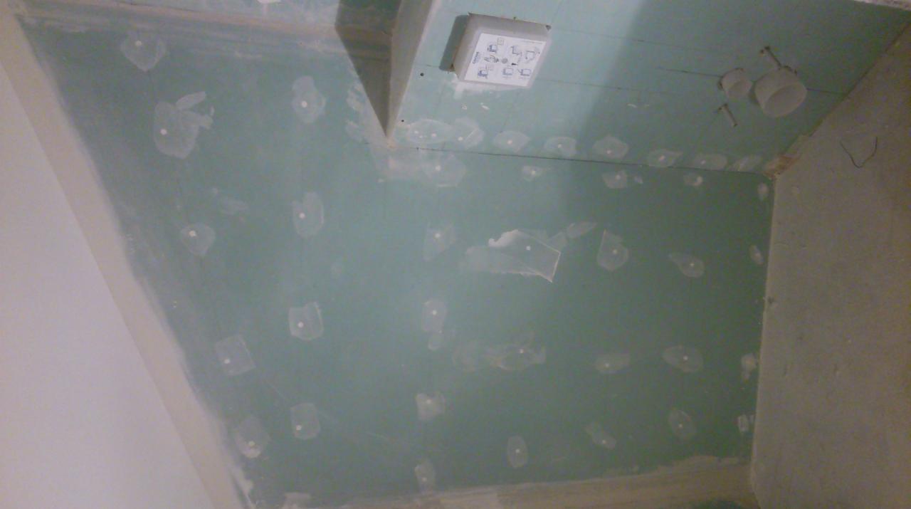 Płyta gipsowo-kartonowa na ścianie i suficie, z widocznymi miejscami po wkrętach zaklejonymi taśmą, w trakcie szpachlowania, z widoczną puszką elektryczną i fragmentem instalacji wodnej.