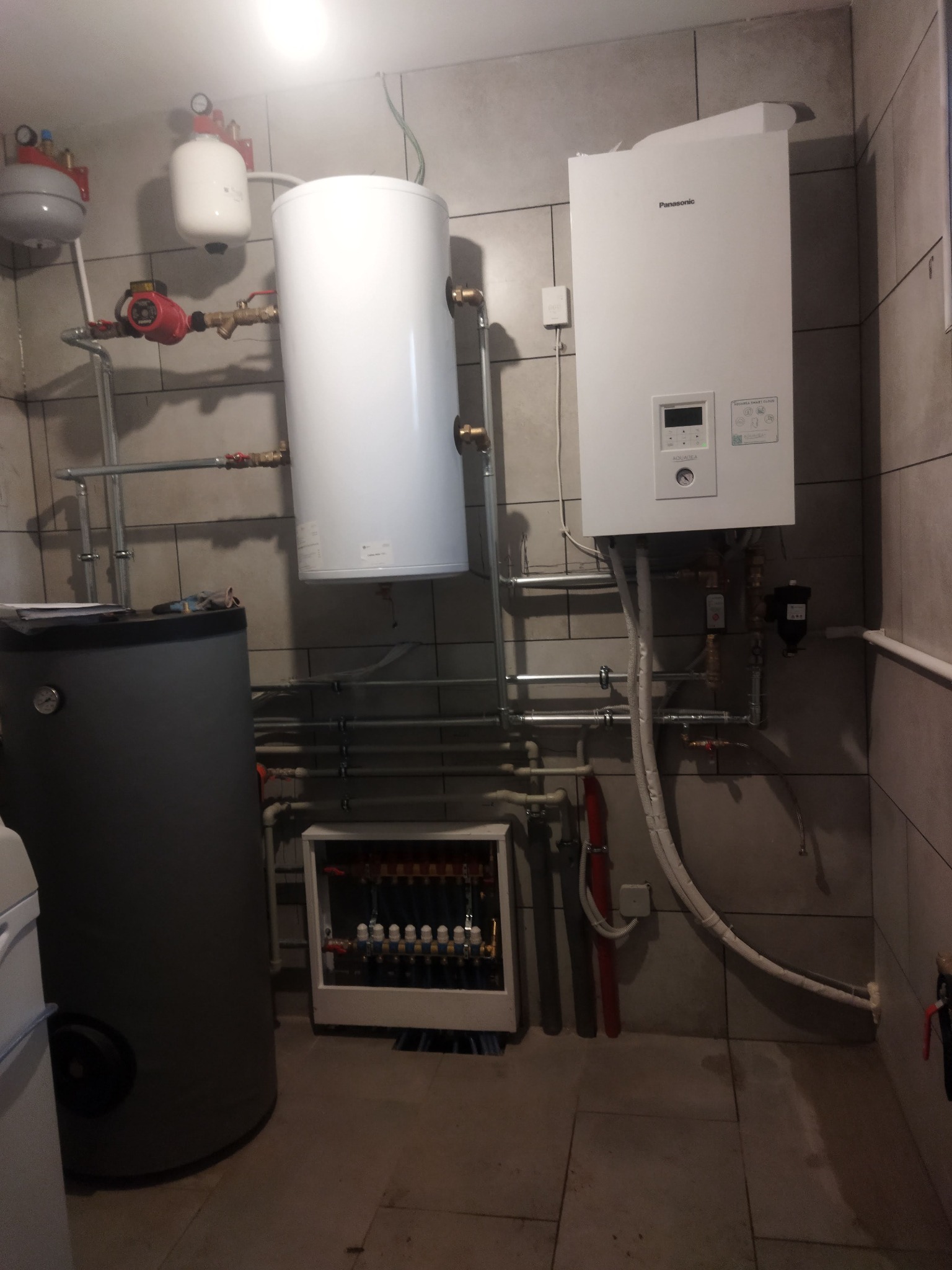 Instalacja grzewcza z zasobnikiem, kotłem gazowym Panasonic Aquarea i rozdzielaczem podłogówki w pomieszczeniu technicznym w Białobrzegach, widoczne liczne rury i zawory.