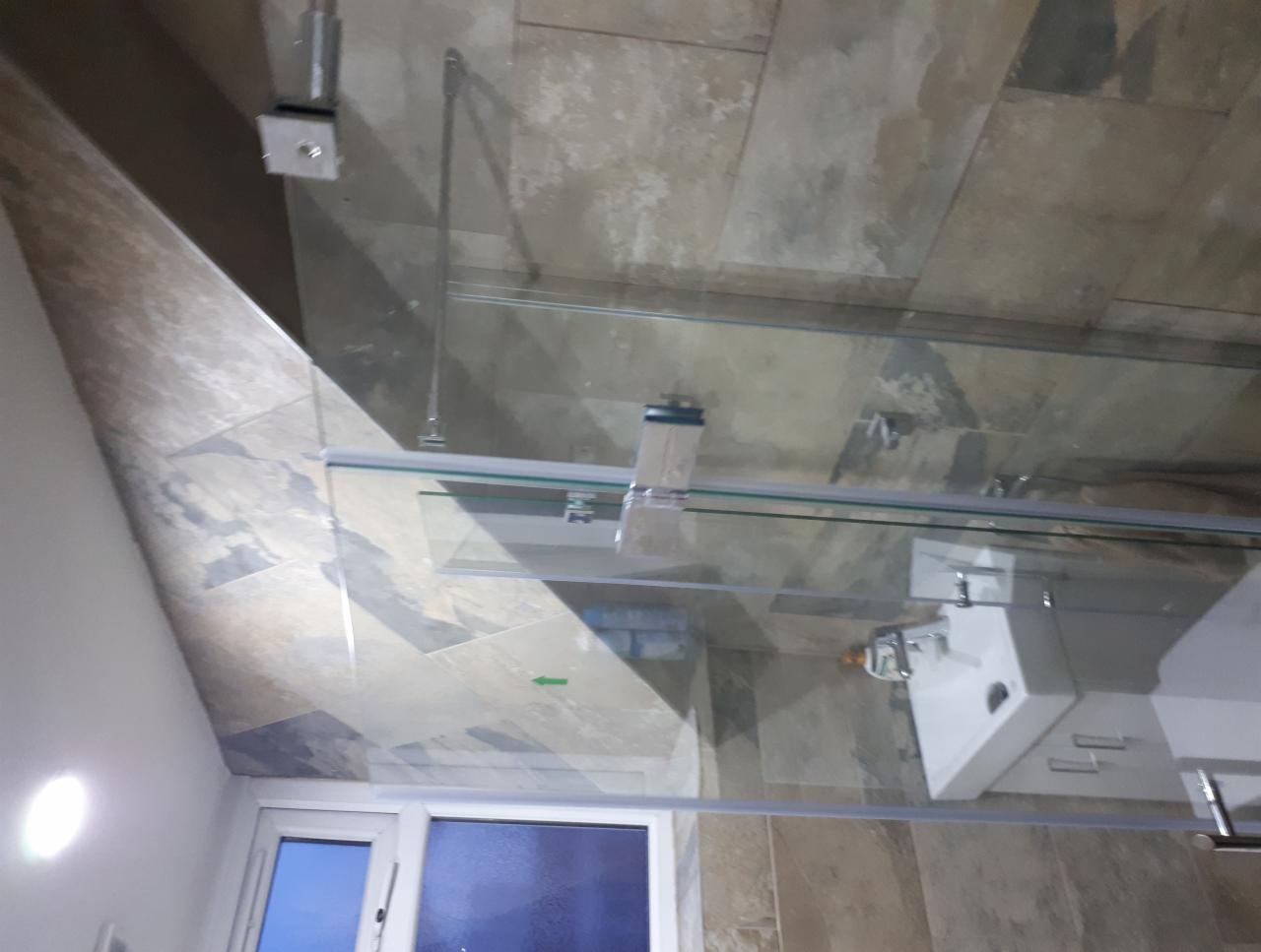 Nowoczesna łazienka z kabiną prysznicową ze szklanymi ściankami i umywalką nablatową, wykończona płytkami imitującymi kamień w odcieniach szarości i beżu, widok na okno.