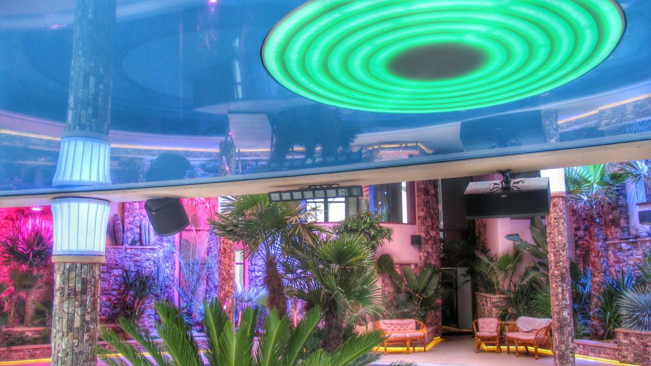 Egzotyczne wnętrze z podświetlanym sufitem napinanym w kształcie okręgów, kamiennymi kolumnami z oświetleniem i roślinami tropikalnymi.