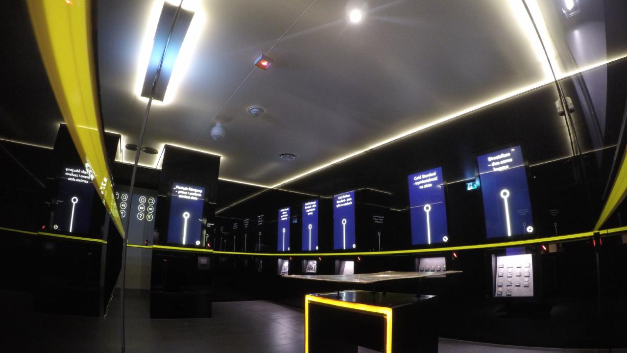 Nowoczesne oświetlenie liniowe LED w ciemnym pomieszczeniu wystawienniczym z interaktywnymi ekranami.