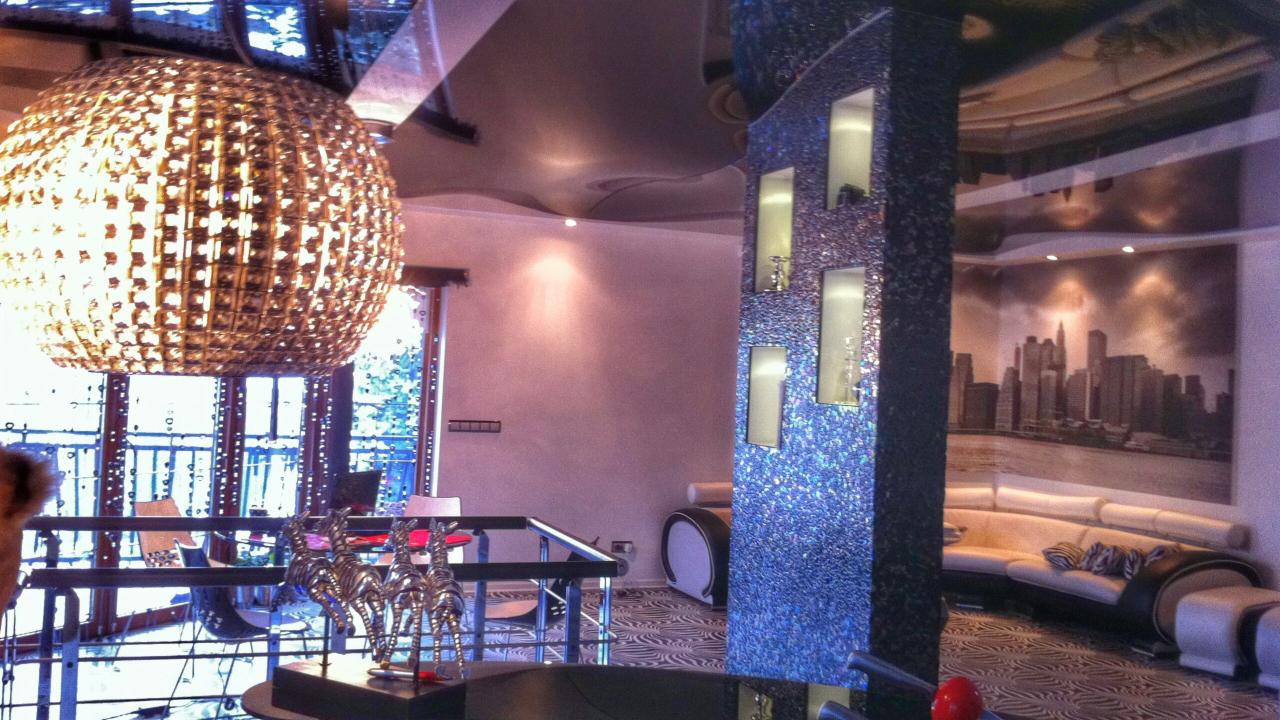 Nowoczesne wnętrze z kulistą lampą wiszącą, dekoracyjną kolumną z oświetleniem wnękowym i fototapetą z panoramą miasta.