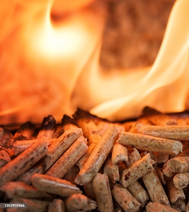 Płonące drewniane granulki w palenisku, widoczne płomienie ogrzewające biopaliwo.