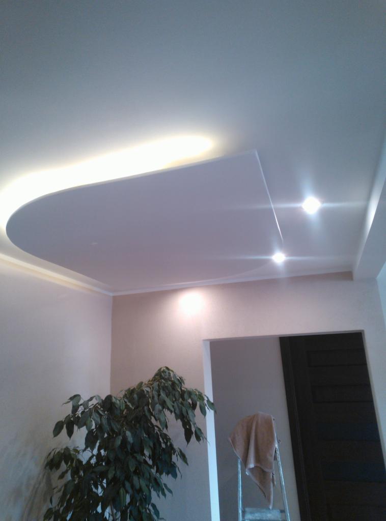 Nowoczesny sufit podwieszany z oświetleniem LED, widoczny fragment pokoju z rośliną doniczkową i drabiną z ręcznikiem.