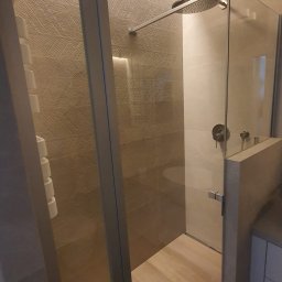 FACH- LUX Jeremiasz Kolankiewicz - Nowoczesna kabina prysznicowa z deszczownicą i szklanymi drzwiami, wykończona płytkami imitującymi drewno na ścianach i podłodze, z widocznym grzejnikiem drabinkowym.