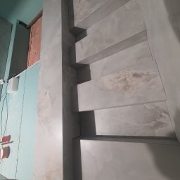 FACH- LUX Jeremiasz Kolankiewicz - Wykończenie ściany z półkami z płytek imitujących marmur w trakcie prac, widoczna płyta kartonowo-gipsowa i elementy instalacji elektrycznej.