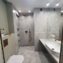 Nowoczesna łazienka z płytkami imitującymi marmur, armaturą w kolorze miedzi i umywalką nablatową o owalnym kształcie, widoczne niedokończone prace wykończeniowe przy zabudowie toalety.