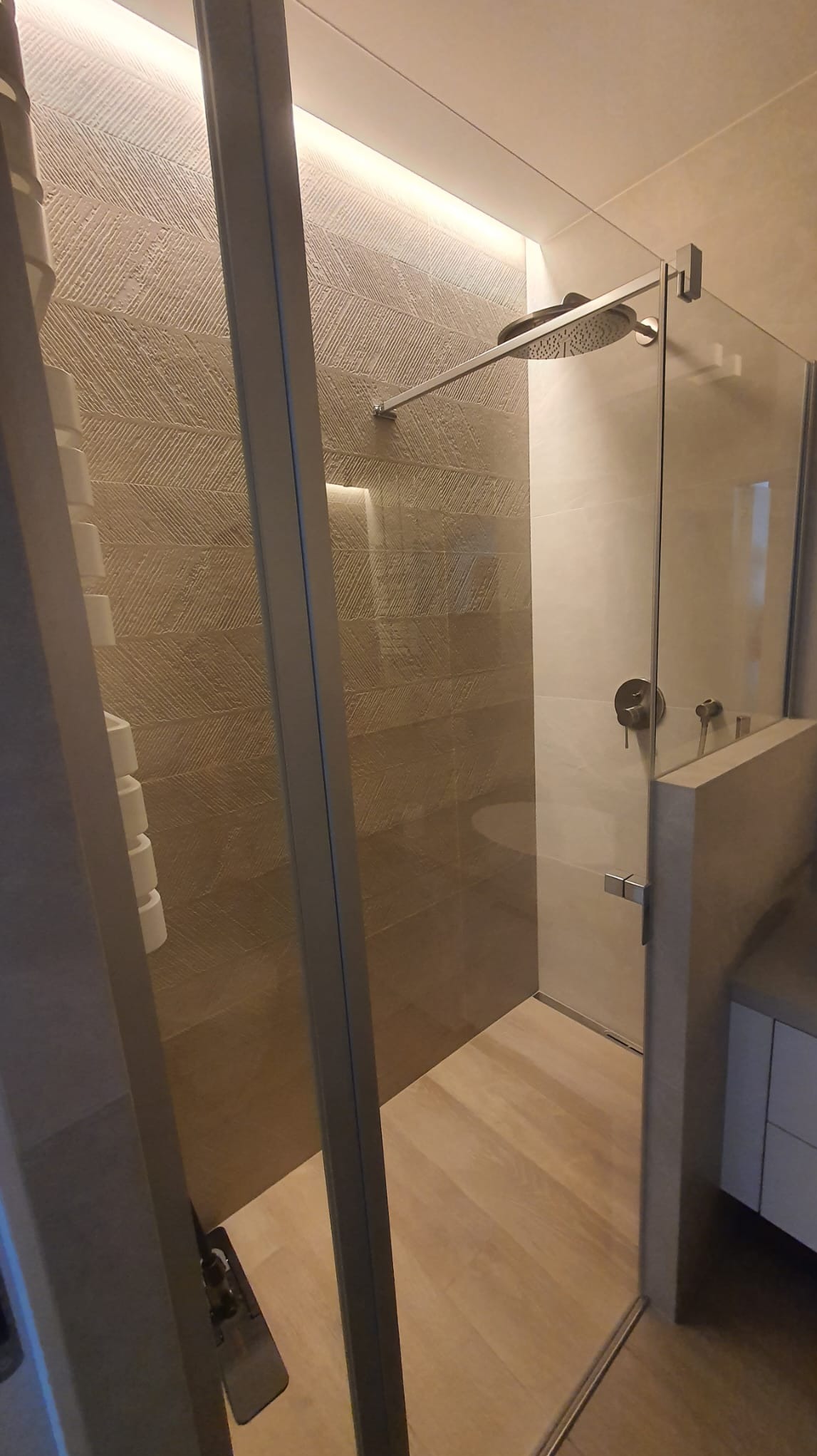 Nowoczesna kabina prysznicowa z deszczownicą i szklanymi drzwiami, wykończona płytkami imitującymi drewno na ścianach i podłodze, z widocznym grzejnikiem drabinkowym.