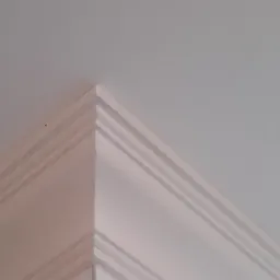 Wykończenie narożnika sufitu z dekoracyjnymi listwami, pomalowane na biało, widoczne z bliska, z niedoskonałościami w postaci drobnych zabrudzeń.