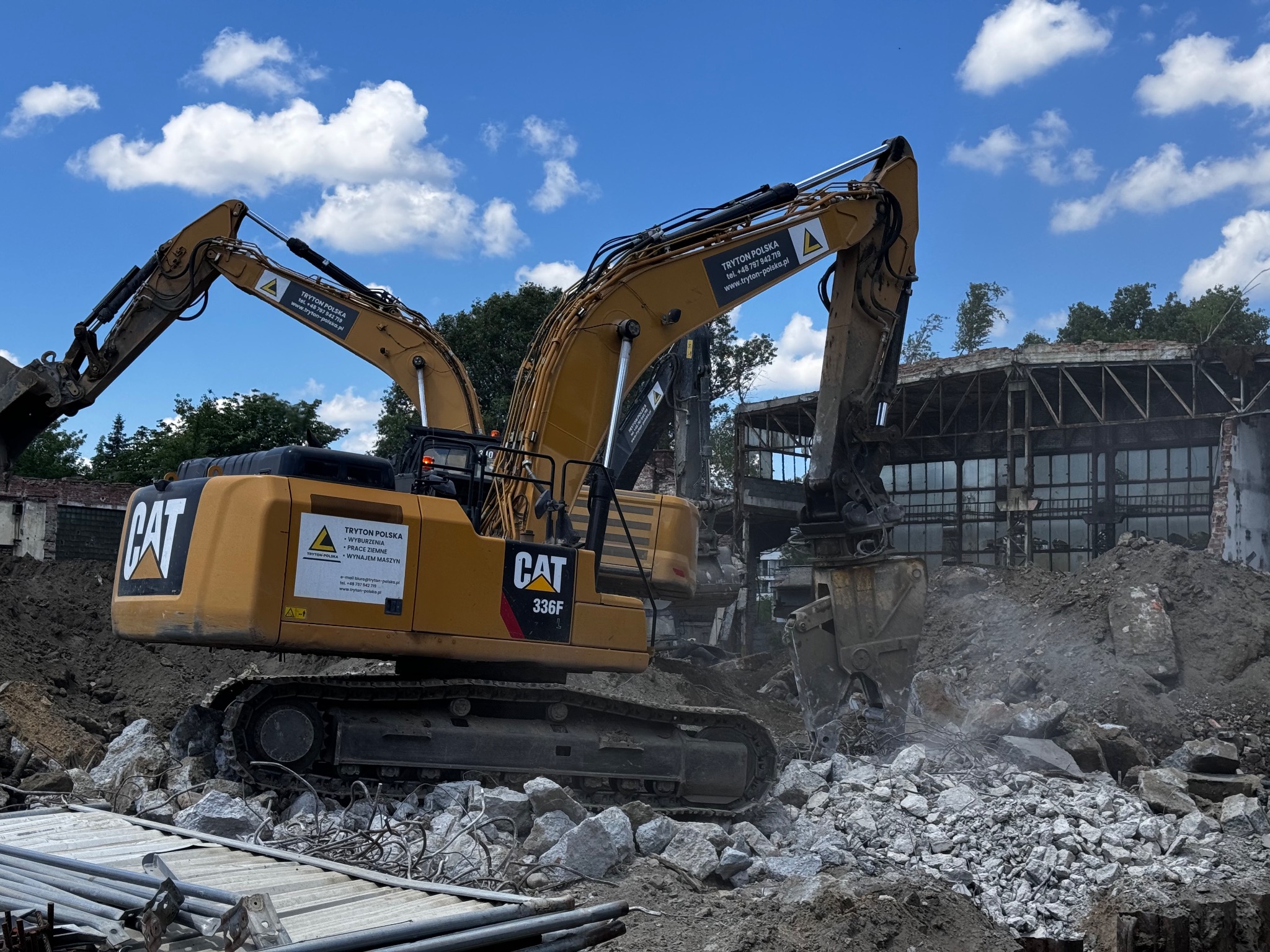 Dwa żółte, gąsienicowe ekskawatory CAT 336F na gruzowisku po rozbiórce budynku, widoczne logo firmy Tryton Polska na maszynach, błękitne niebo z białymi chmurami w tle.