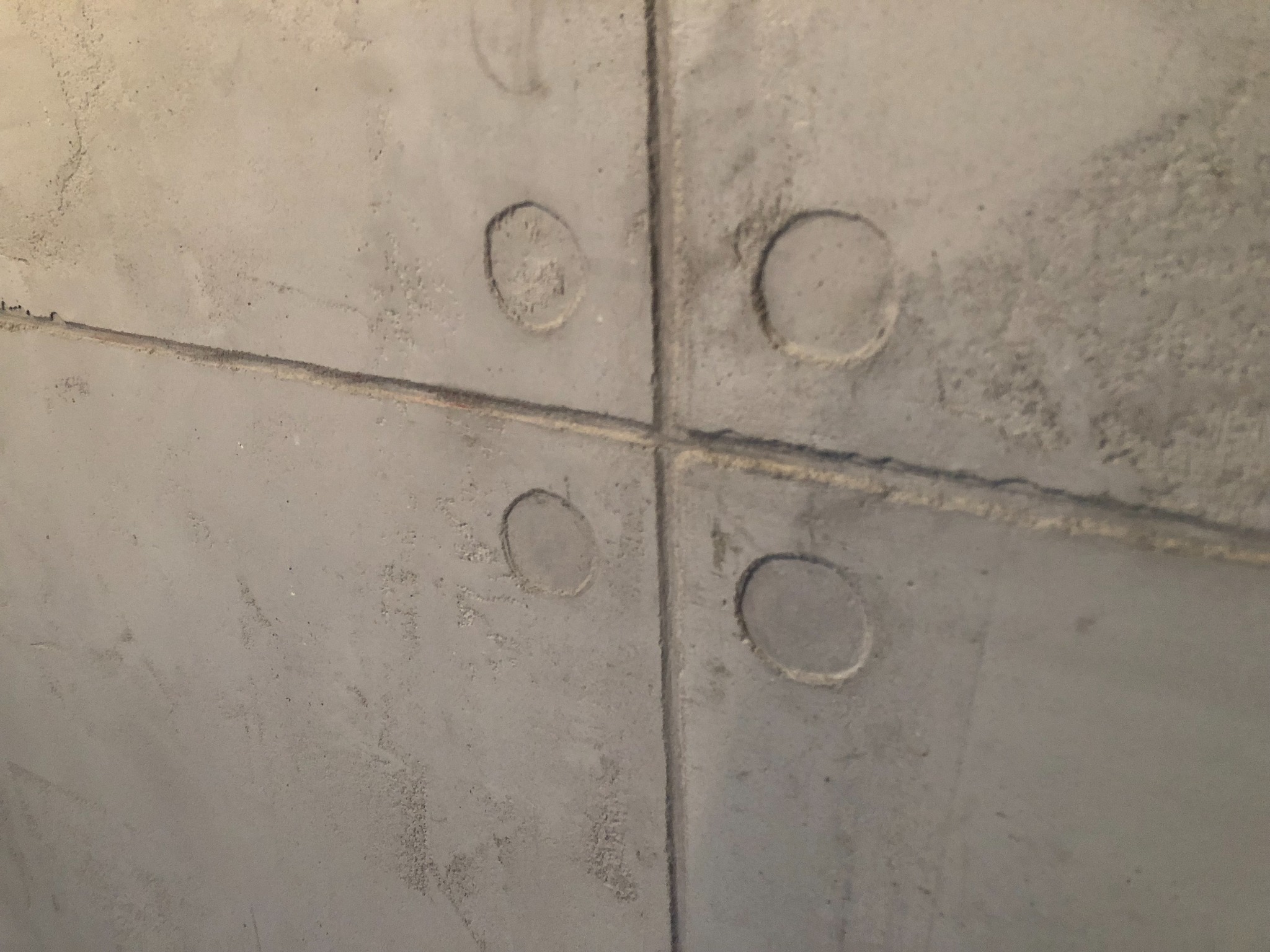 Surowa, szara ściana z betonu komórkowego, podzielona na cztery panele z widocznymi, okrągłymi wgłębieniami po szalunkach.