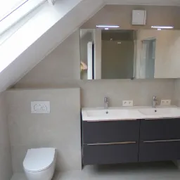 Nowoczesna łazienka na poddaszu z dwoma umywalkami, szarą szafką podumywalkową, wiszącą toaletą i dużym lustrem z oświetleniem LED