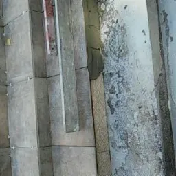 Świeżo położone, szare płytki podłogowe z krzyżykami dystansowymi, widoczne przygotowanie do fugowania, obok surowa ściana w trakcie remontu.