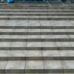 Kamienne schody zewnętrzne z widocznym fragmentem niebieskiej plandeki ochronnej i metalową barierką w tle.