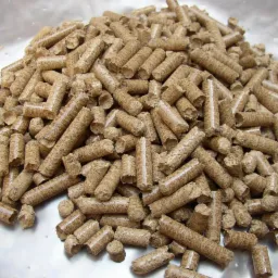 G&oacute;ra jasnobrązowego pelletu drzewnego z widoczną strukturą wł&oacute;kien, ułożona na błyszczącej, lekko zarysowanej powierzchni.