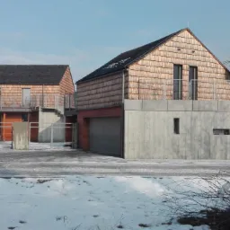 Dwa nowoczesne domy z elewacją z drewnianych płytek, betonowymi fundamentami i metalowymi balustradami, widok z zewnątrz w zimowej scenerii.