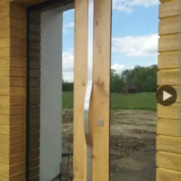 Nowoczesne, przesuwne, drewniane drzwi zewnętrzne z metalowym uchwytem, widok na ogród i dom z zewnątrz.