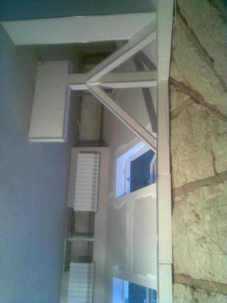 Poddasze w trakcie adaptacji: widoczne krokwie z izolacją z wełny mineralnej, metalowa konstrukcja wzmacniająca, płyty gipsowo-kartonowe przygotowane do montażu przy oknach dachowych.