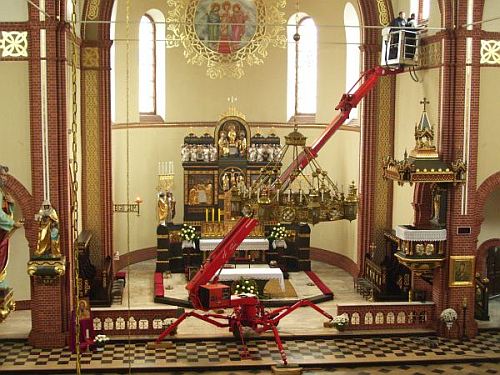 Czerwony podnośnik koszowy wewnątrz kościoła podczas prac konserwatorskich przy żyrandolu i suficie.