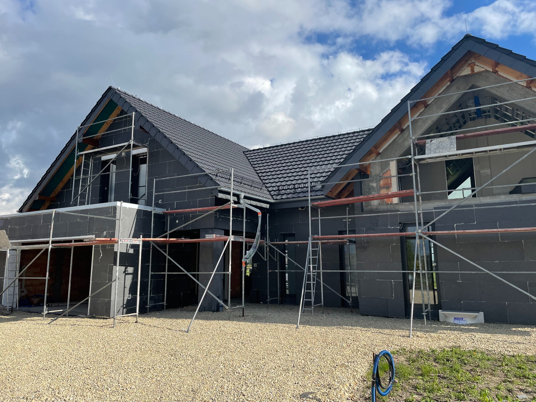 Dom w trakcie budowy z czarną elewacją i grafitowym pokryciem, widoczne rusztowania i elementy konstrukcji dachu.