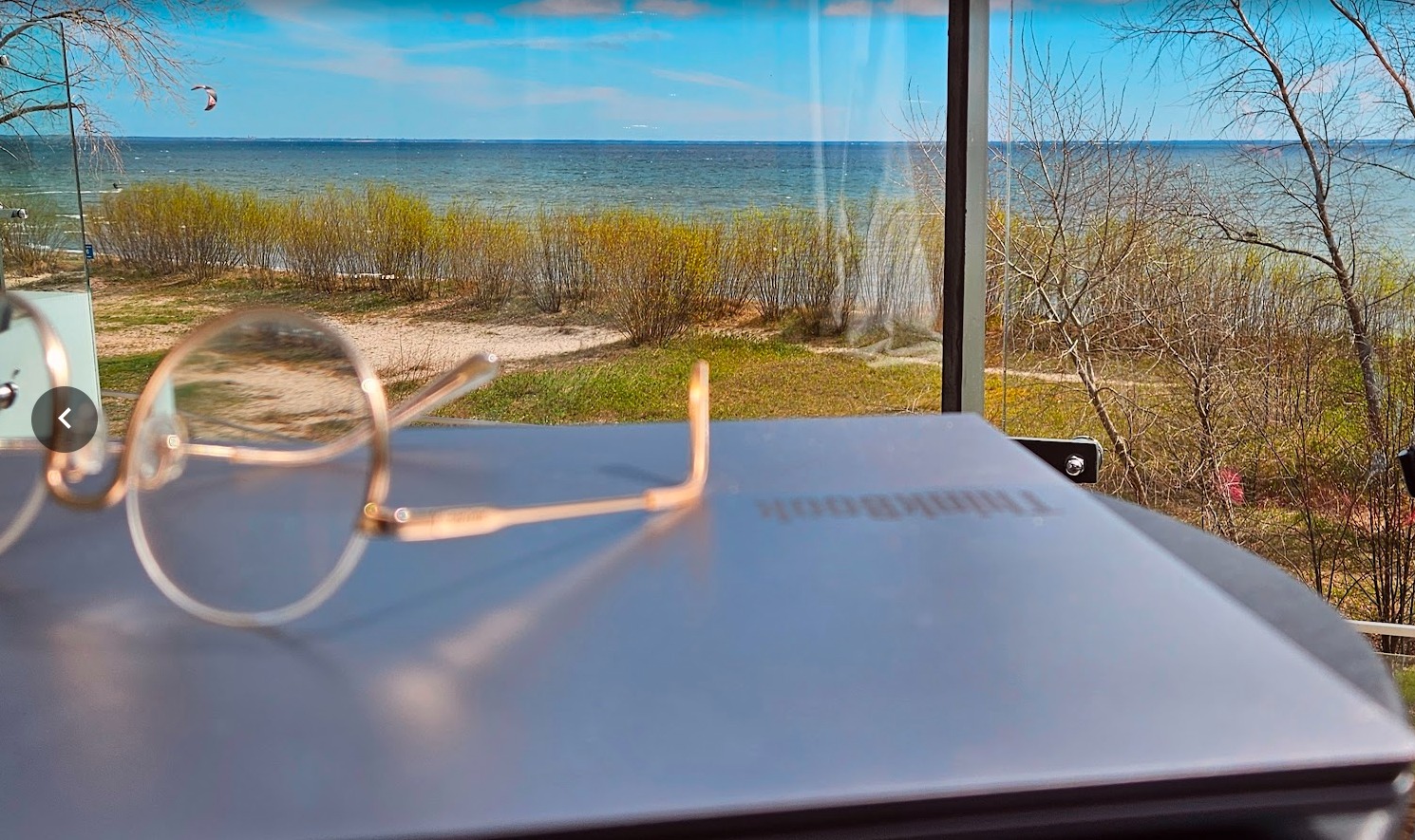 Laptop ThinkBook z okularami na tle widoku na morze, sugerujący relaks podczas nauki angielskiego online.